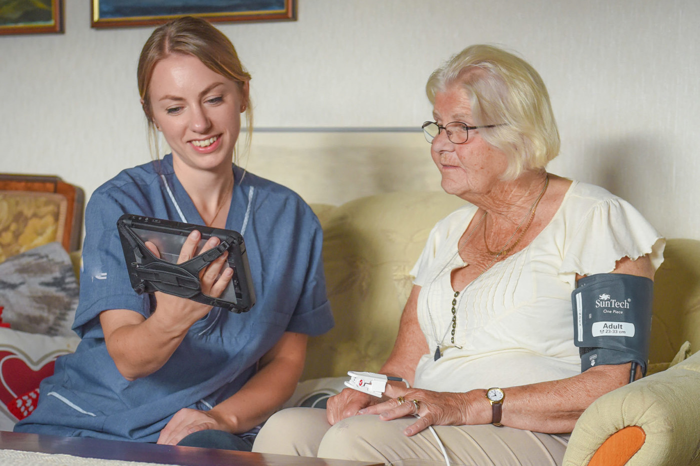 Sjuksköterska i hemmet med MobiMed monitor som visar en patient de vitala värdena